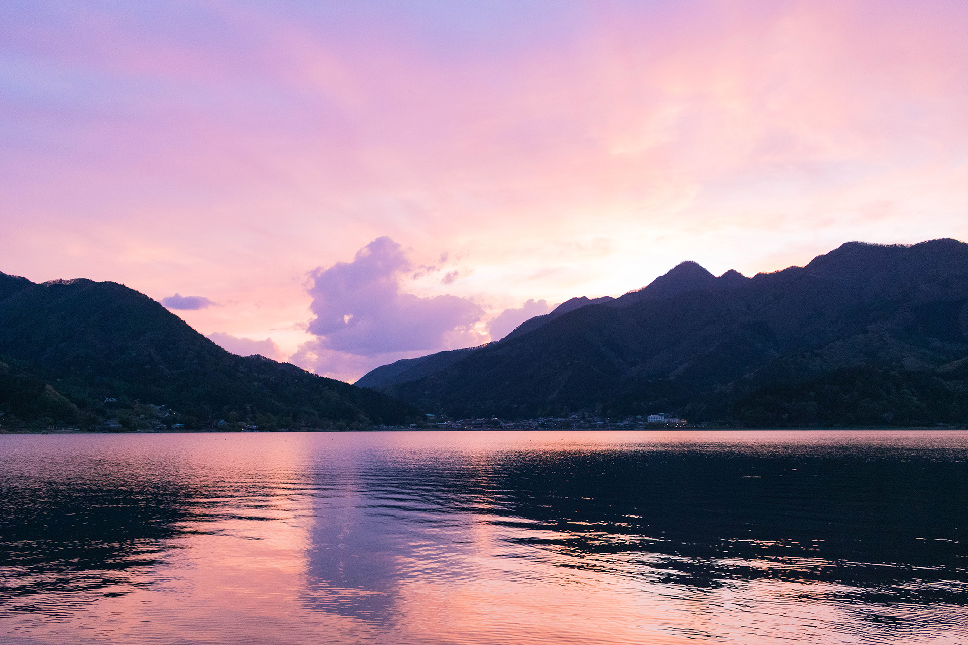 Vibrant sunset behind a mountain with a lake at the base.